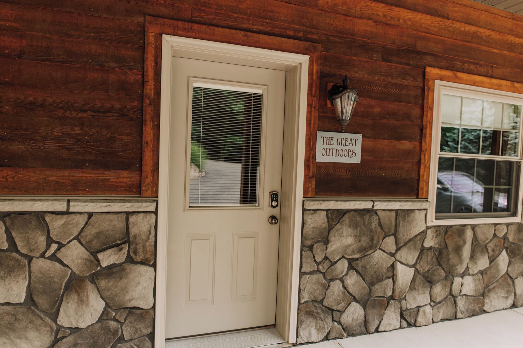 A wooden exterior with a stone foundation, a door with a window, and a sign reading "THE GREAT OUTDOORS".