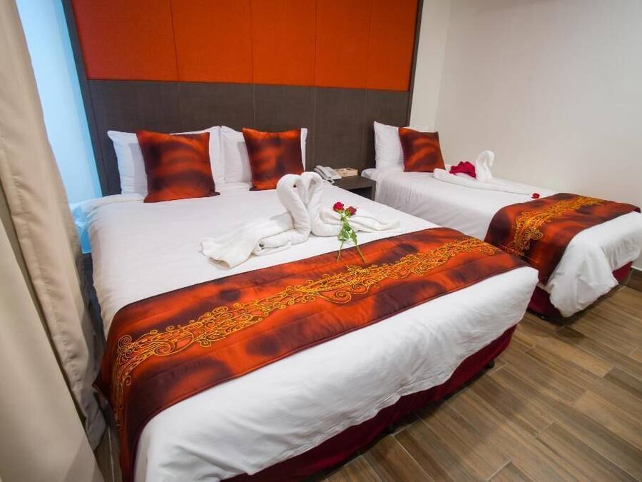 A hotel room with two beds, each with white linens and red accents, a wooden floor, and a modern headboard.