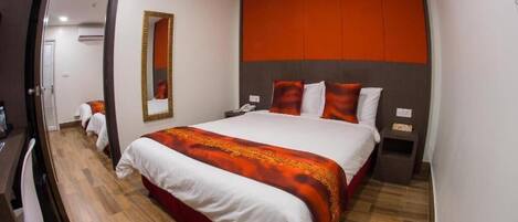 A hotel room with a large bed, a mirror, a bedside table, and a door leading to another room.