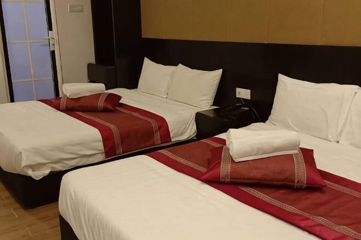 Quarto de hotel com duas camas, cada uma com roupa de cama branca e almofadas decorativas vermelhas.