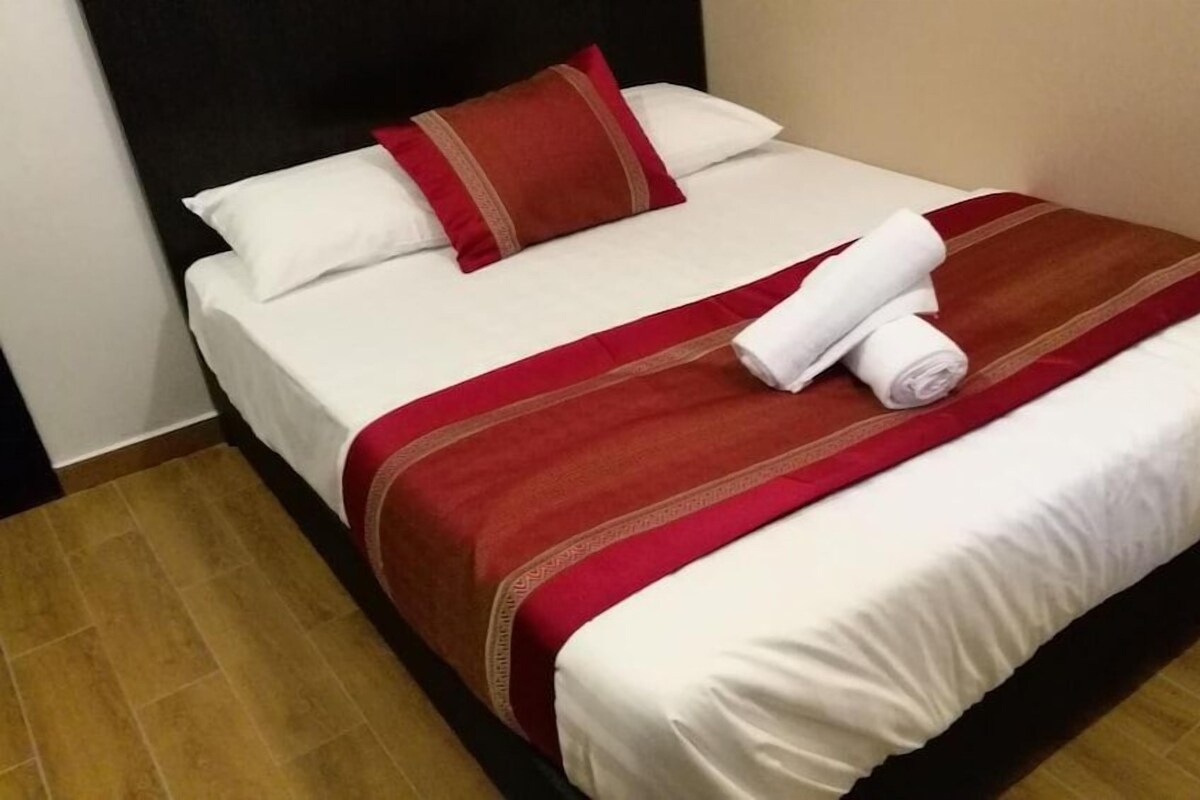 Ett hotellrum med en säng, kuddar och en hoprullad handduk.