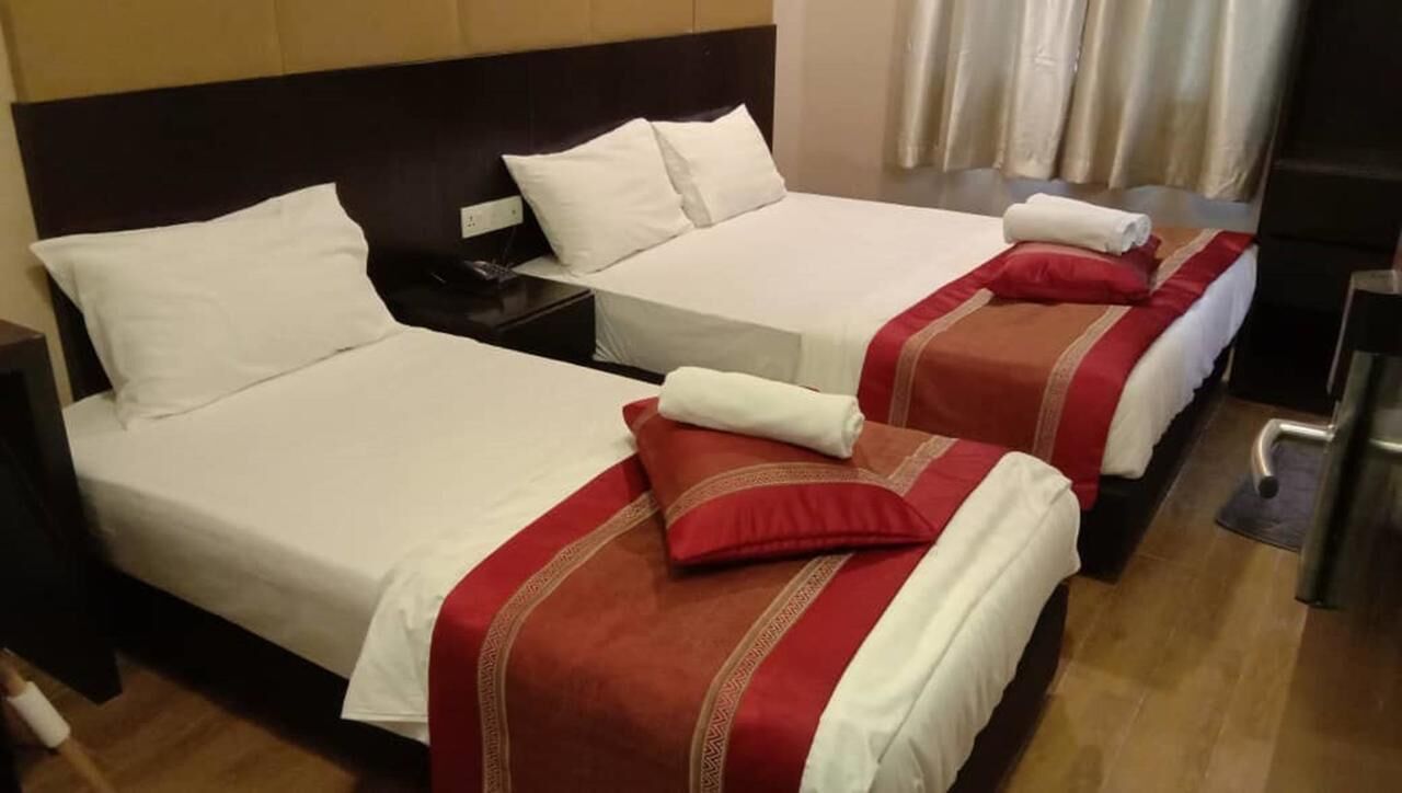 A hotel room with two beds, each with white bedding and red accents. There are bedside tables with lamps and a small table between the beds.