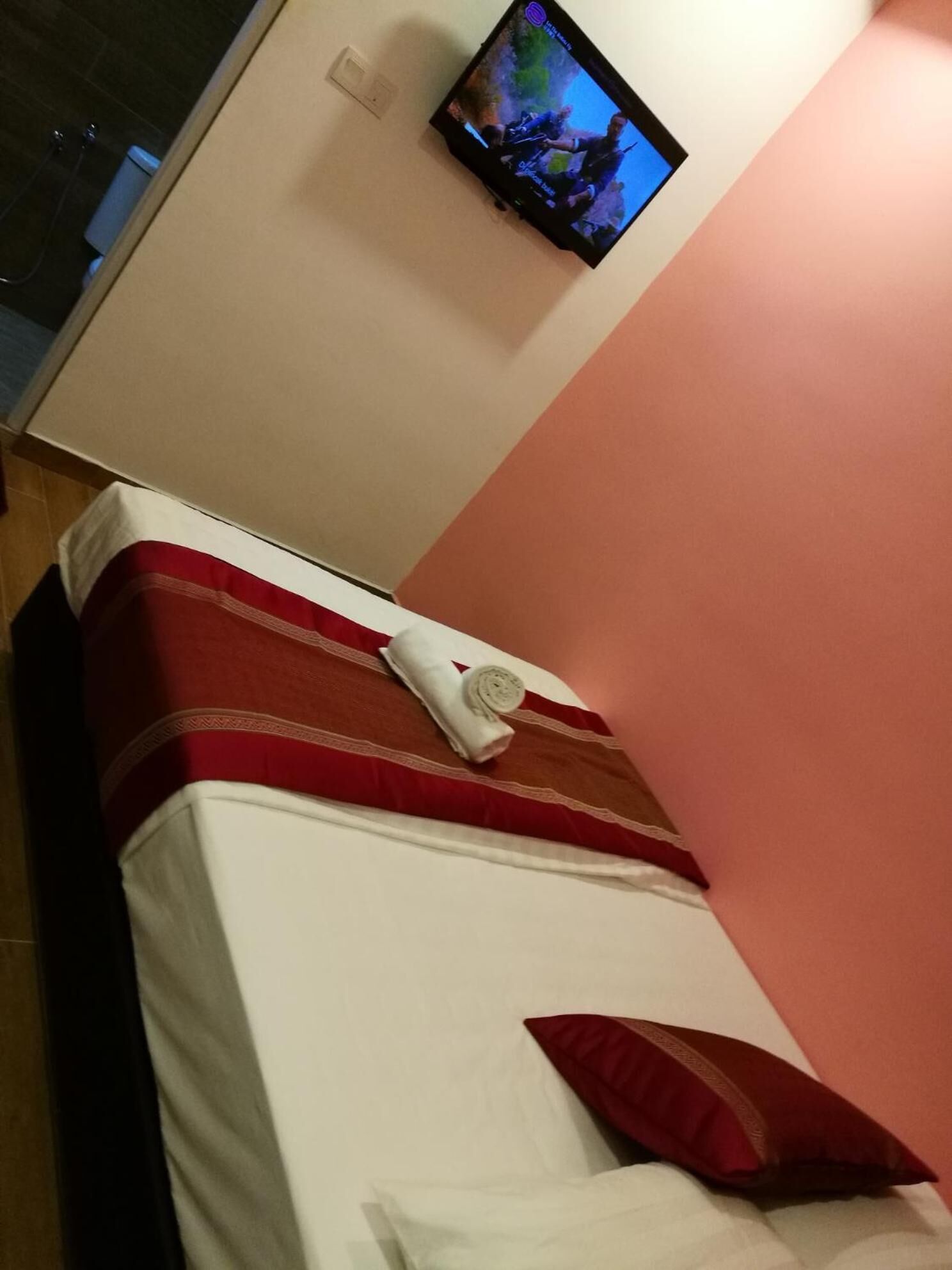 Une chambre d’hôtel avec un lit, un téléviseur fixé au mur et une salle de bain visible au fond.