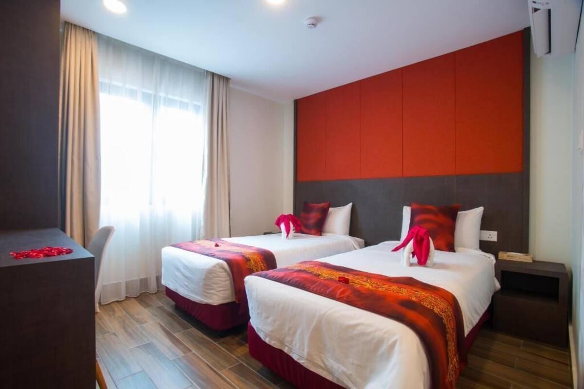 Quarto de hotel com duas camas, uma mesa e uma janela com cortinas.