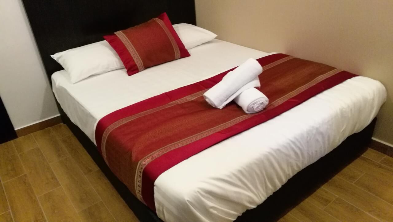 A neatly made bed with white linens and a red and brown striped blanket, a red pillow, and two rolled white towels on the bed.