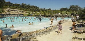 Ein großer Pool im Freien, umgeben von Liegestühlen und Sonnenschirmen, mit Felsen im Hintergrund und Palmen.