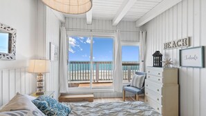 Un dormitorio con una cama grande, un aparador, una silla y vista a la playa a través de una puerta corrediza.