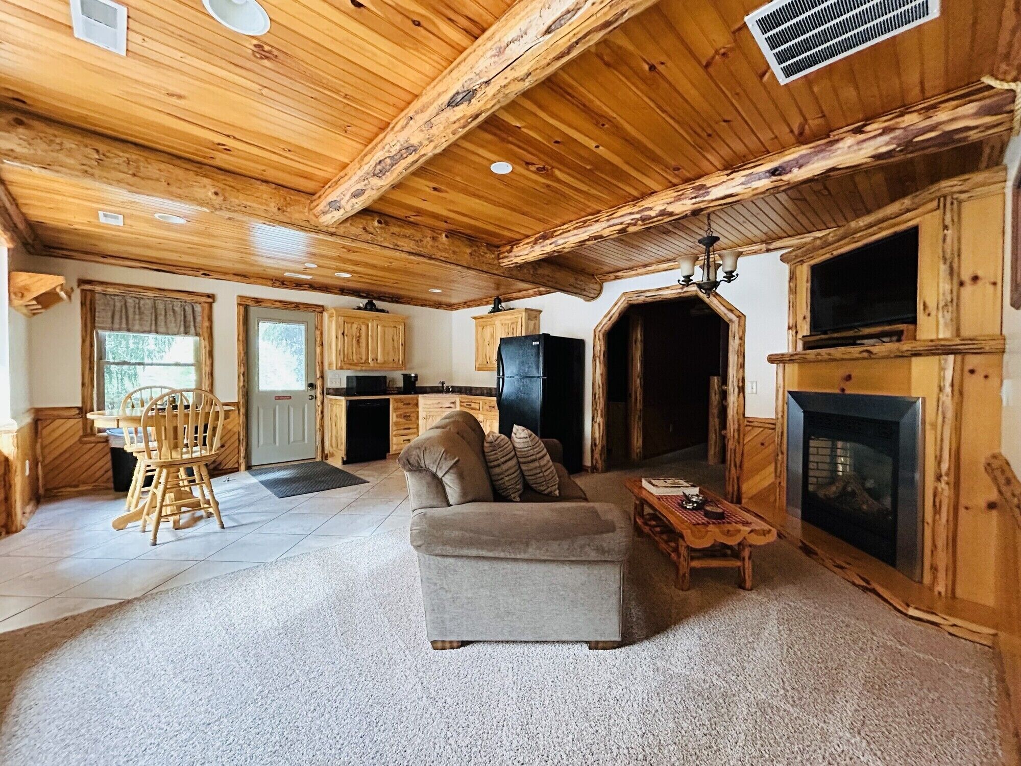 A rustic cabin interior with a living room, kitchen, and fireplace.