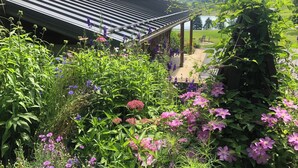 Un jardín con diversas flores y una casa de techo inclinado.