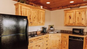 Una cocina con armarios de madera, un refrigerador negro, una cafetera, un microondas y un lavavajillas.
