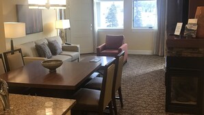 A hotel room with a dining area, a fireplace, a large window with a view of trees, and a carpeted floor. - Luxury One Bedroom Westin Riverfront Villa (Avon)