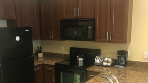 A kitchen with dark wooden cabinets, a black refrigerator, a microwave, a stove, and a granite countertop with a stainless steel sink. - Luxury One Bedroom Westin Riverfront Villa (Avon)