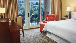 A hotel room with a bed, a desk, a chair, and a view of a mountainous landscape through large glass doors. - Luxury One Bedroom Westin Riverfront Villa (Avon)