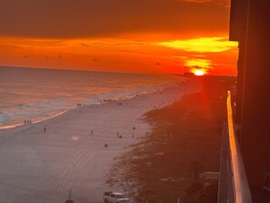 A beach with people walking and a sunset in the background.