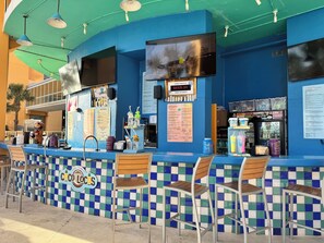 Eine Coco Locos Bar mit einer blau-grün karierten Wand, einem digitalen Bierangebot und einer Speisekarte.
