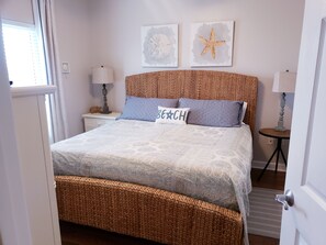 A neatly arranged bedroom with a woven headboard, a bed with patterned bedding, two wall-mounted lamps, and a small bedside table with a lamp.