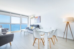 A modern living room with a glass table and chairs, a sofa with cushions, a floor lamp, and a large window overlooking the sea. - Santa Margarita 14-C (Benidorm)