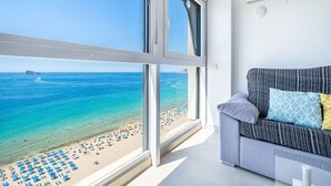Una stanza con una grande finestra vista spiaggia, un divano grigio con cuscini fantasia e un condizionatore d'aria bianco a parete.