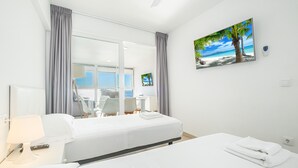 Habitación de hotel con cama, escritorio, silla, televisión y un cuadro de una playa.