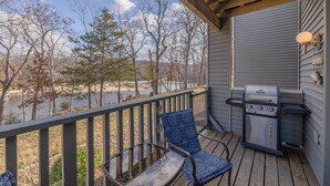 A deck with a grill and a chair, overlooking a body of water and trees. - Lake Aspen Landing by Innsbrook Vacations! (Innsbrook)