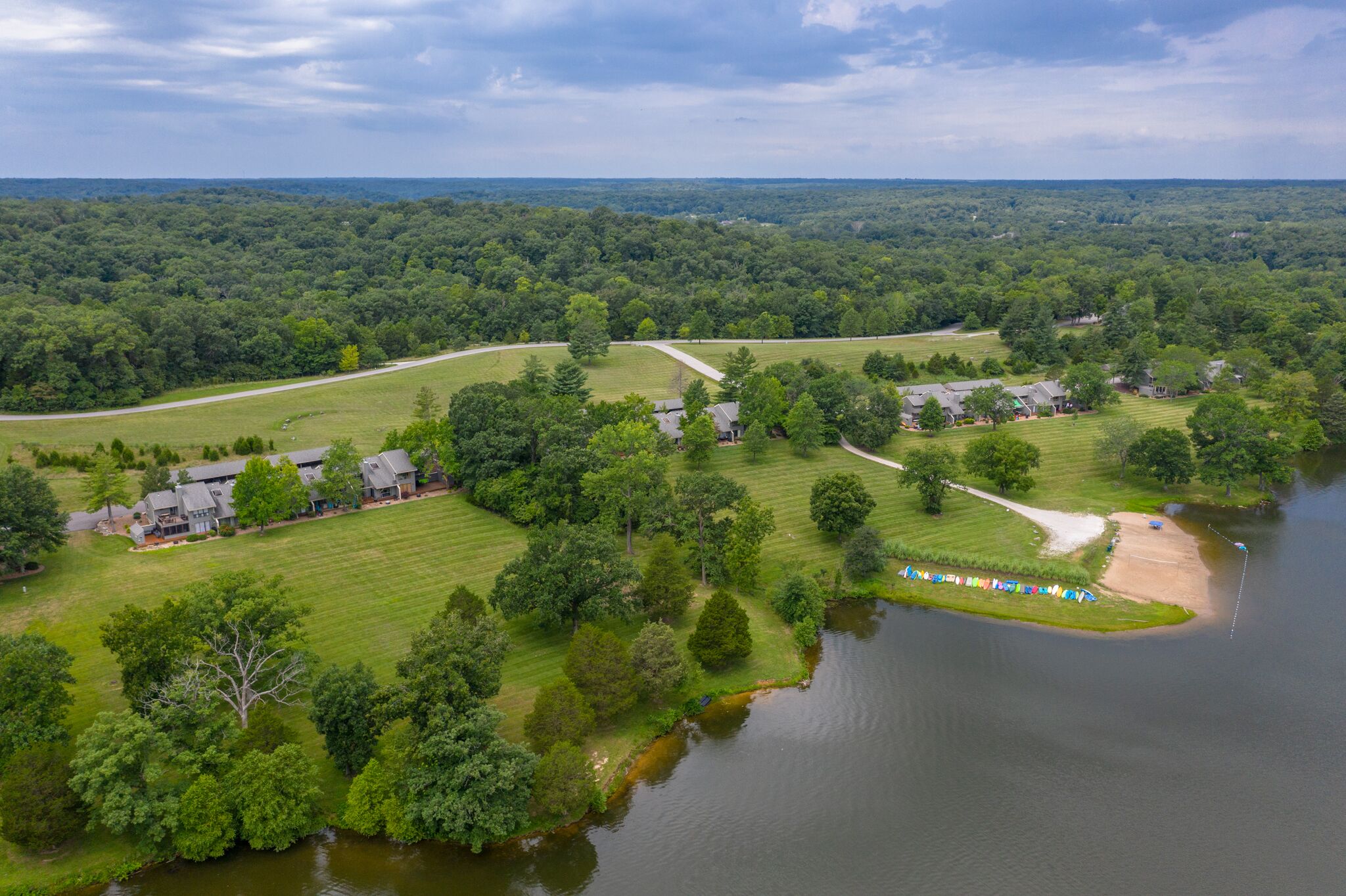 An aerial view of a residential area with houses, a lake, and a forested landscape.