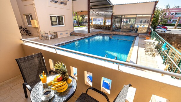 A balcony with a pool, a table with fruit and a drink, and a chair. - Sun Beach Apartments (Chania)