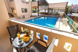 Un balcón con piscina, una mesa con fruta y una bebida, y una silla.