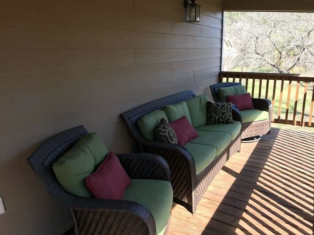 Ein überdachter Außenbereich mit Korbmöbeln und Kissen, einer Holzterrasse und Blick auf Bäume.
