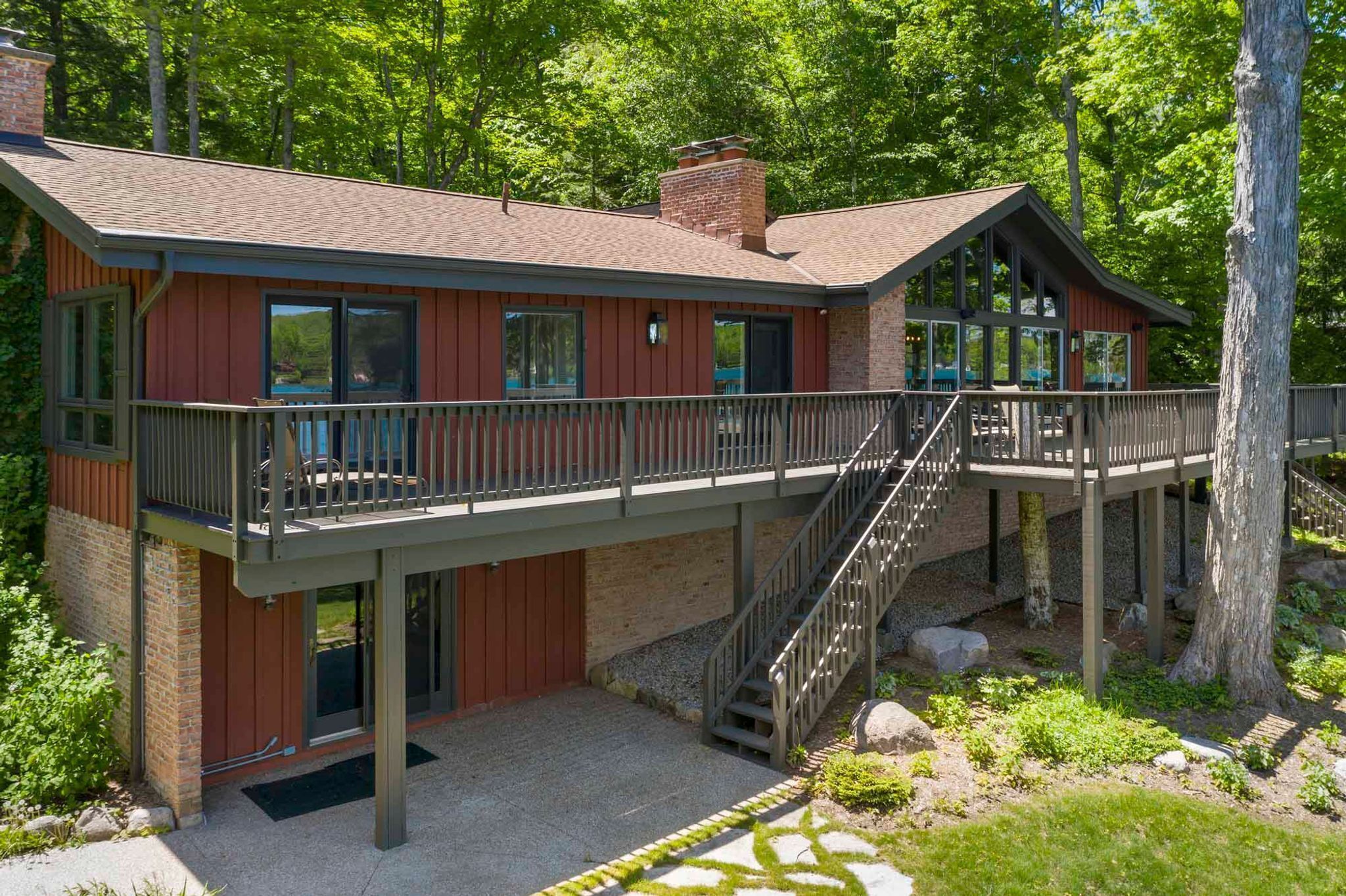 A two-story cabin with a balcony and a deck, surrounded by trees.