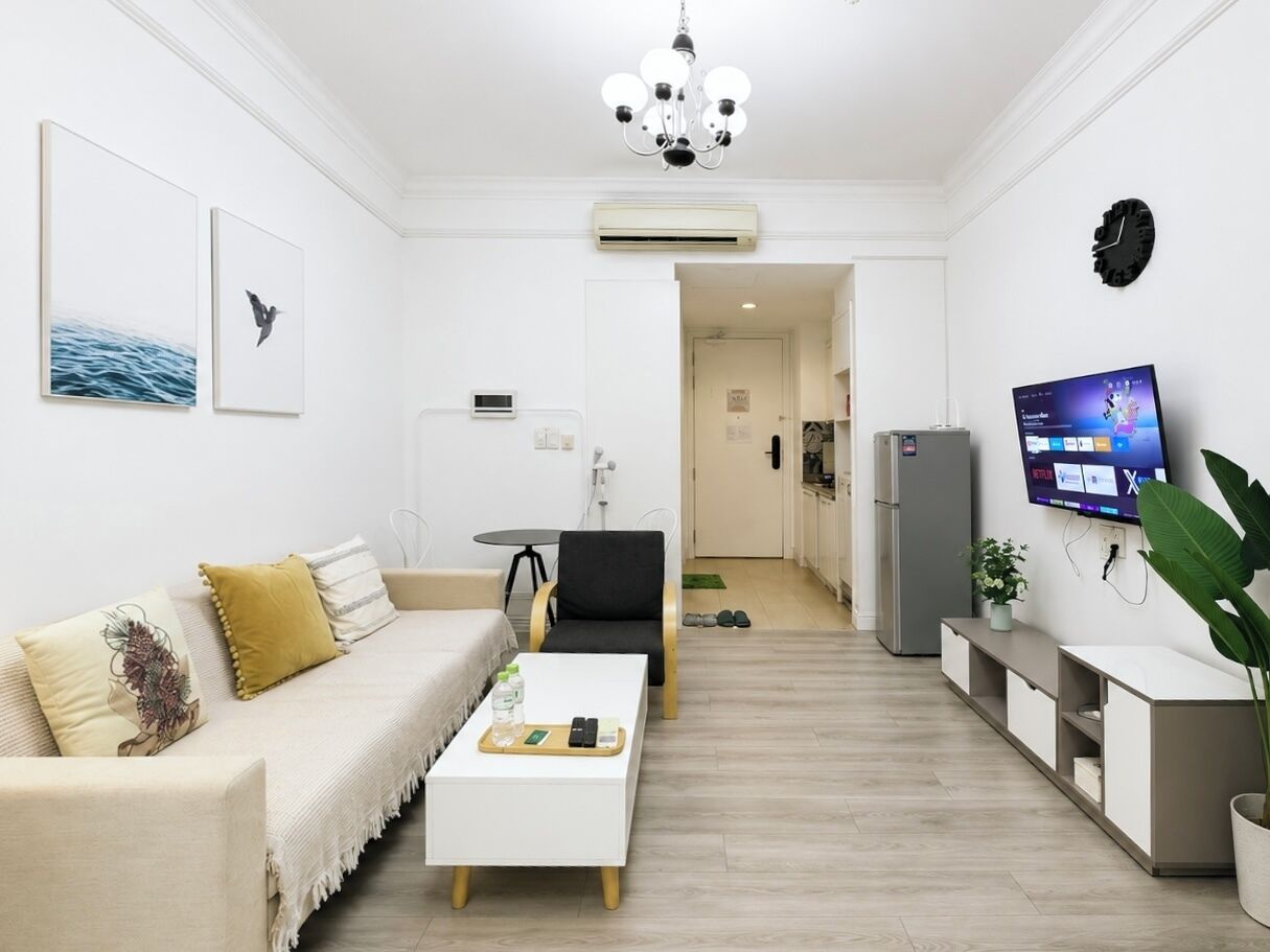 Una sala de estar moderna con un sofá, una mesa de centro, un televisor y una cocina al fondo.