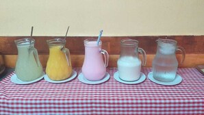 A table with five pitchers of different colored beverages on a checkered tablecloth. - Pousada Ilson (Olímpia)