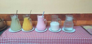 A table with five pitchers of different colored beverages on a checkered tablecloth. - Pousada Ilson (Olímpia)