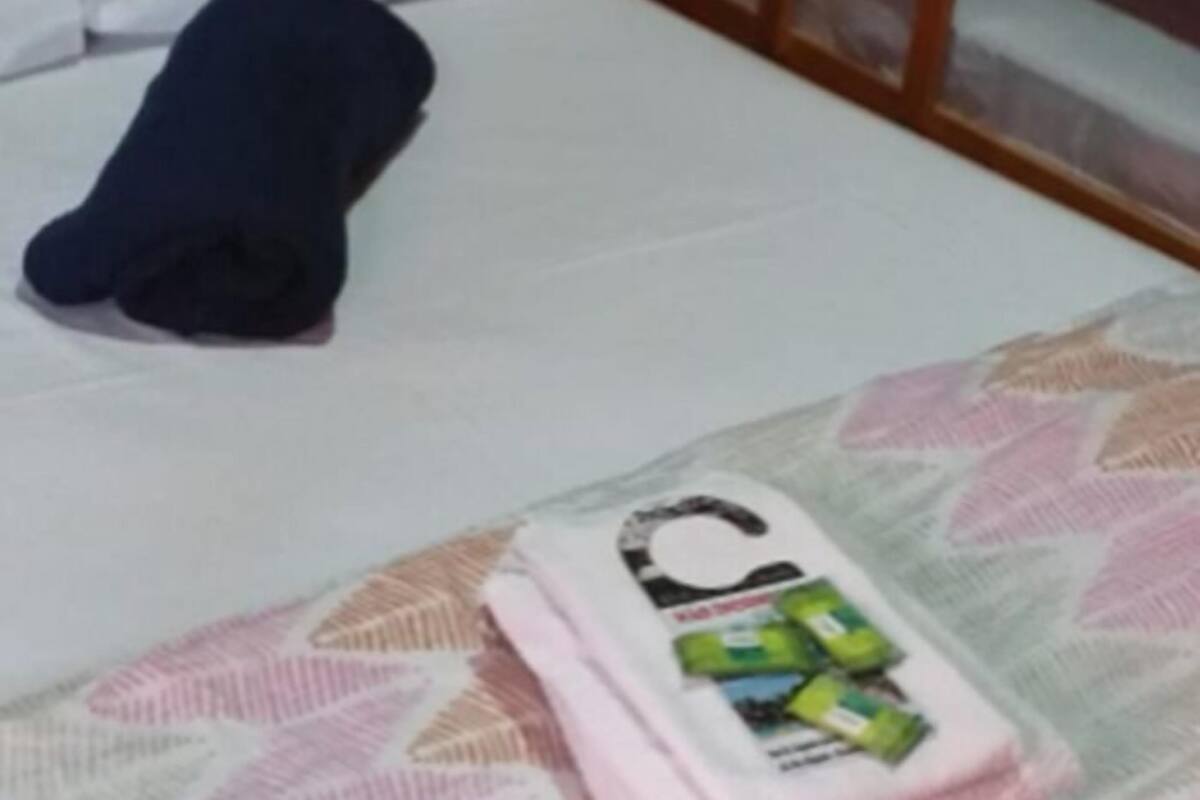 A bed with a white sheet, a folded towel, and a blanket with a leaf pattern.