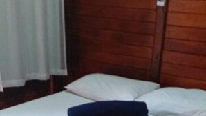 A single bed with a patterned bedspread and a blue pillow, wooden headboard, and a white curtain. - Pousada Ilson (Olímpia)