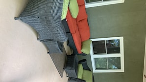 A room with a grey woven sofa set, green and red cushions, and a window with blinds. - Quiet sunsets on Lanier (Oakwood)