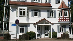 A white two-story house with a red-tiled roof, multiple windows with shutters, and a small porch area. - Guest house Villa Lina (Bad Herrenalb)