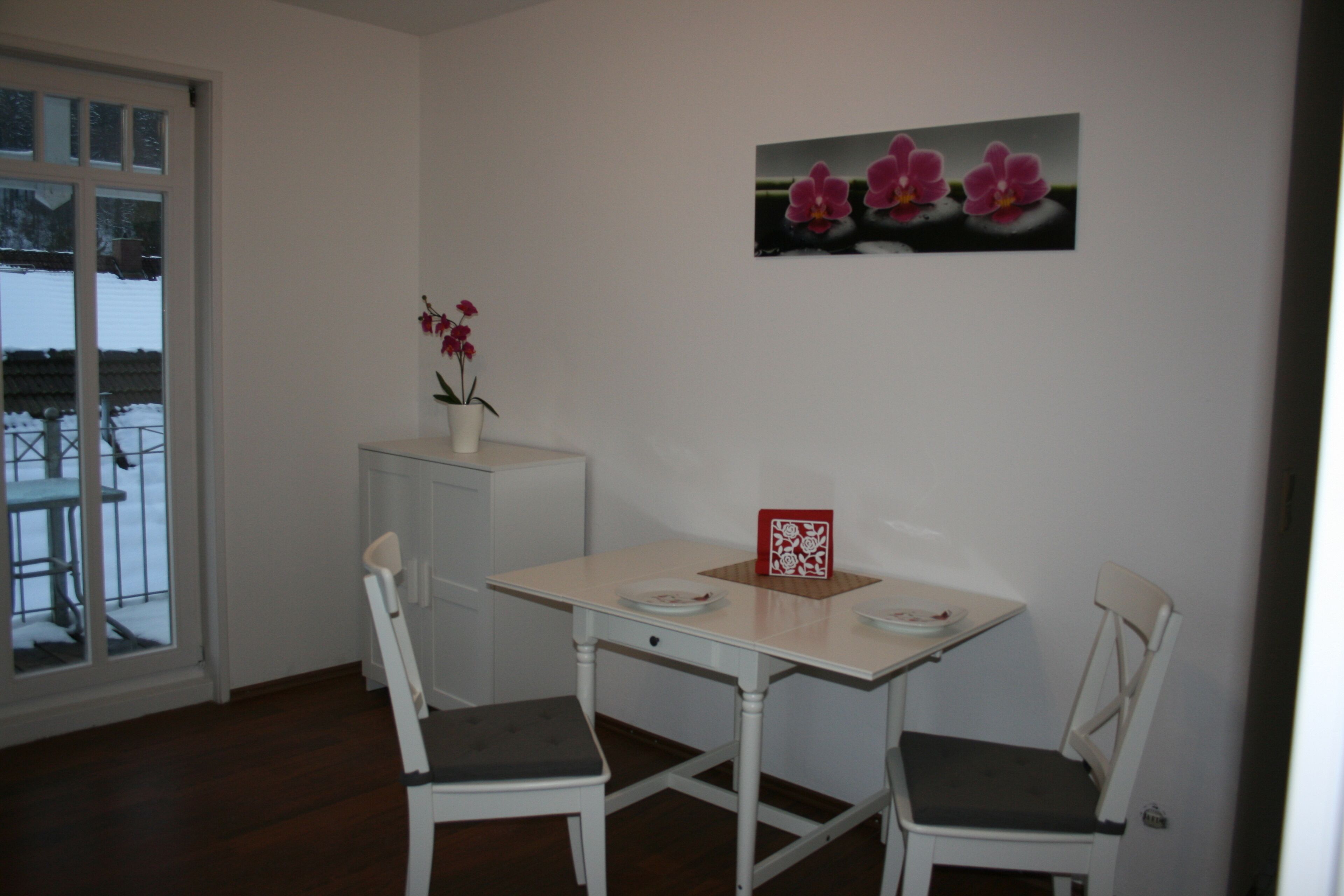 Un coin repas avec une table et deux chaises, une plante en pot et un tableau encadré au mur.