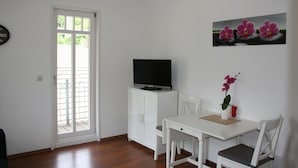 A small, clean room with a white table, two chairs, a television on a cabinet, and a door leading to a balcony. - Guest house Villa Lina (Bad Herrenalb)