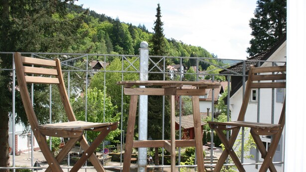 A wooden deck with two chairs and a table, surrounded by a metal fence, overlooking a residential area with houses and trees. - Guest house Villa Lina (Bad Herrenalb)