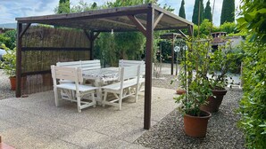 Un'area salotto all'aperto riparata, con tavolo e panche, circondata da ghiaia e piante in vaso.