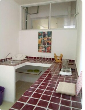 Kitchen area with sink, faucet, and utensils, featuring a colorful fruit-themed artwork.