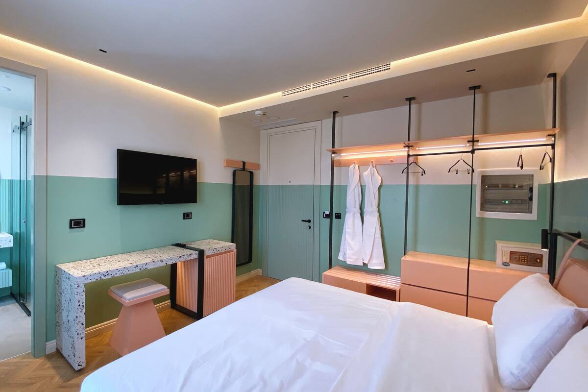 Une chambre d’hôtel moderne équipée d’un lit, d’un bureau, d’une télévision, d’une douche et d’un porte-peignoir.