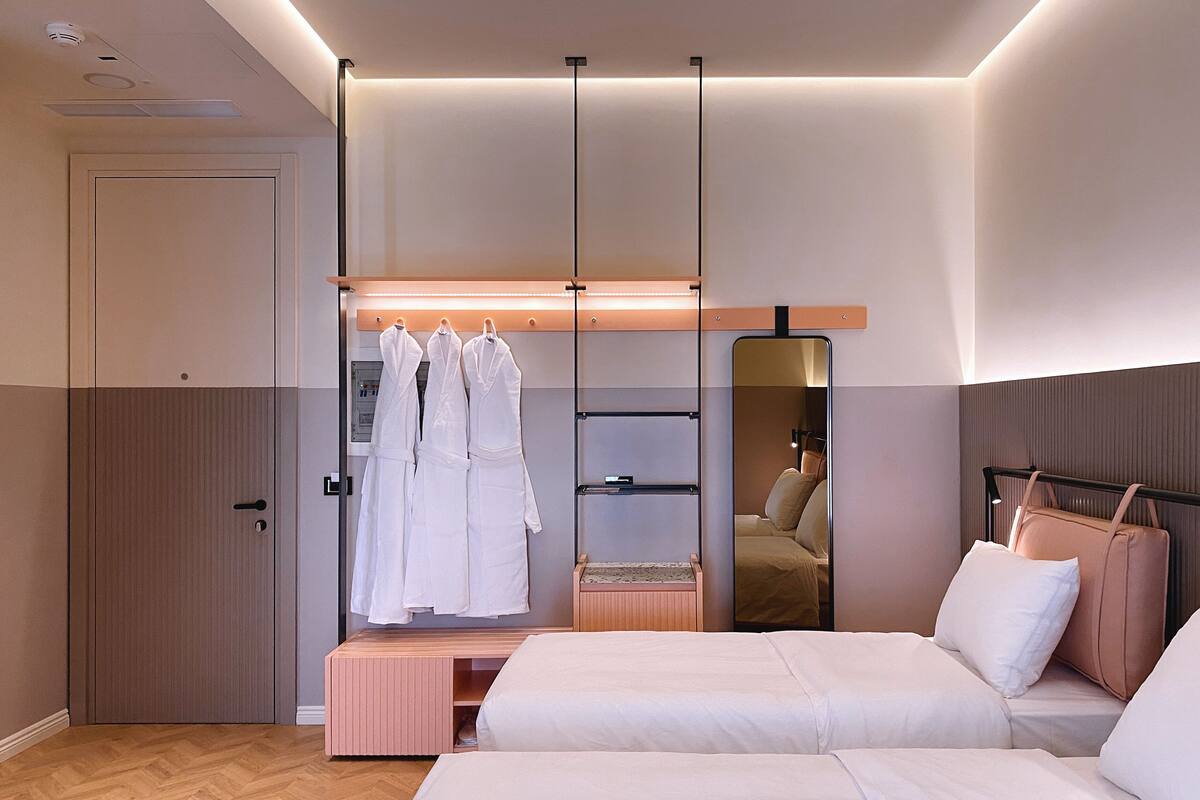 Une chambre d’hôtel moderne avec deux lits, un dressing et un grand miroir.
