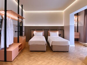 Une chambre d’hôtel avec deux lits, un banc en bois, une armoire et un miroir.