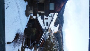 A modern building with a sloped roof, surrounded by snow-covered ground and a forested hillside. - Chalet 6/7 people at the foot of the Pyrenees 2000 slopes in the forest (Bolquère)