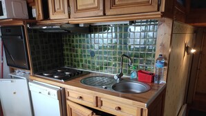 A compact kitchen with wooden cabinets, a stainless steel sink, a stove, and a dishwasher. - Chalet 6/7 people at the foot of the Pyrenees 2000 slopes in the forest (Bolquère)