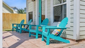 Una casa con porche que muestra dos sillas Adirondack turquesa con cojines coloridos.