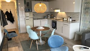 Et kompakt køkken med spiseplads, med et rundt bord, blå stole og en hængende lampe.