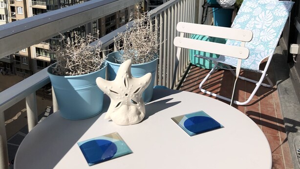 En balkon med et hvidt bord, blå plantekasser, et hvidt pynteting og en loungeseng med et blå og hvidt mønster.