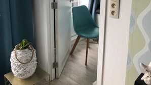 Et værelse med en turkis stol, et lille bord med en plante, og en dør til et andet værelse.